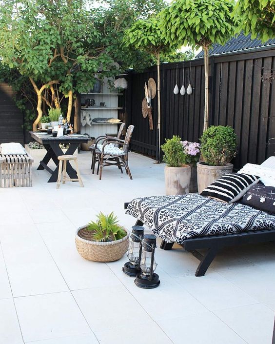 a Scandinavian black and white terrace with stained and black furniture and black and white textiles, potted greenery, some decor and a black fence