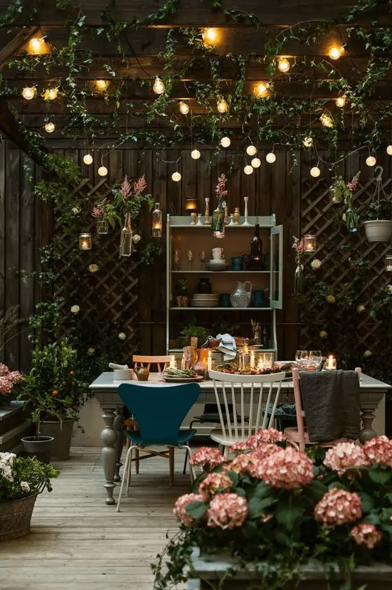 a backyard dining space with string lights over the space and candle lanterns on the table plus florals around