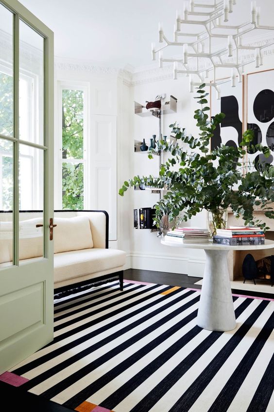 a beautiful black and white living room with a striped rug, a white sofa, a coffee table with greenery, some art and shelves