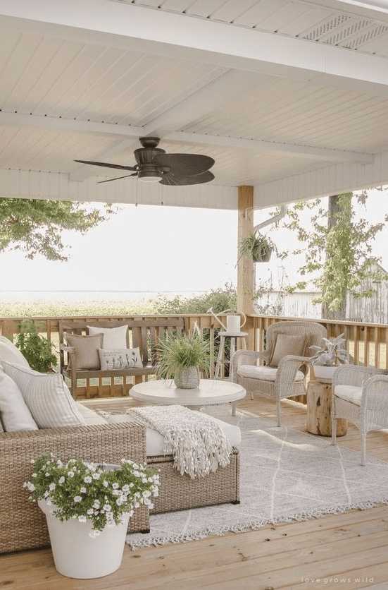 a beautiful neutral modern farmhouse terrace with neutral wicker furniture, a round coffee table, potted plants and blooms