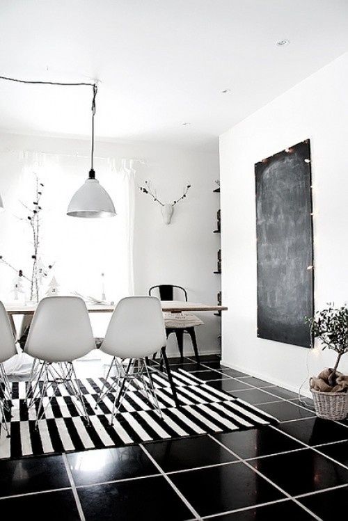 a black and white dining room with a stripe rug, a table with white chairs, a chalkboard, a pendant lamp and some potted plants