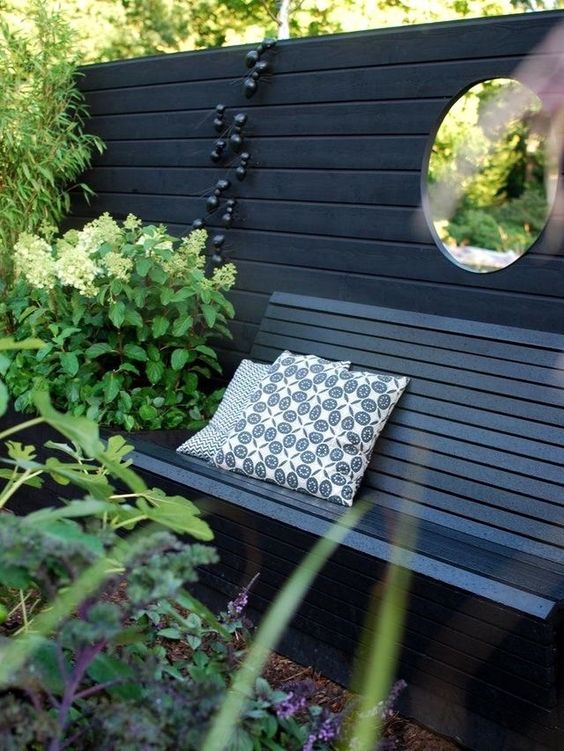 a black fence, a black bench, some greenery and blooms, decorative ants and a round window are a unique combo for outdoors