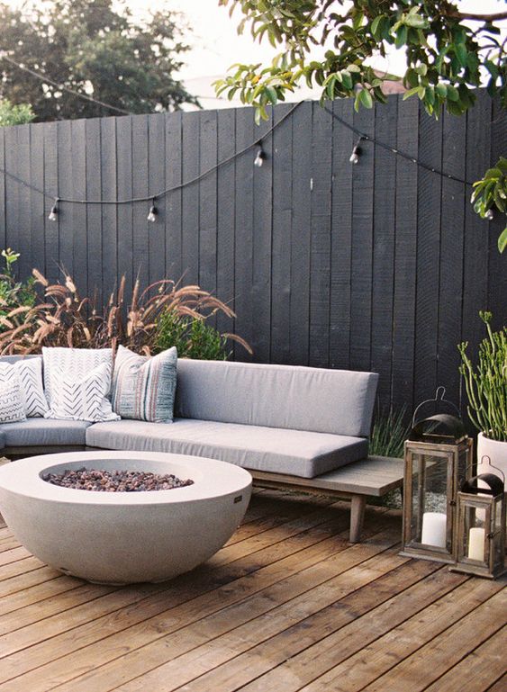 a black fence, a modern grey sofa, a fire bowl, lights and potted plants are a chic combo for a modern terrace