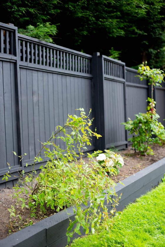 a black fence lined up with a raised garden bed with greenery are a cool combo to rock, green refreshes the space