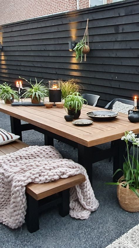 a black fence, modern stained furniture, potted greenery, candles and wall lamps and greenery on the fence are great for a Scandinavian space