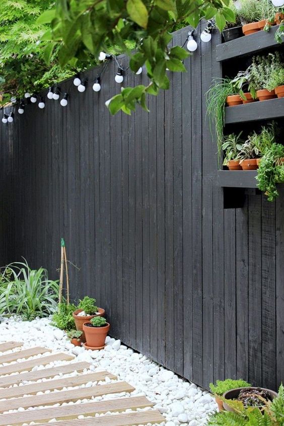 a black fence refreshed with a black shelf with herbs and lights is a cool solution for a modern or Scandinavian terrace
