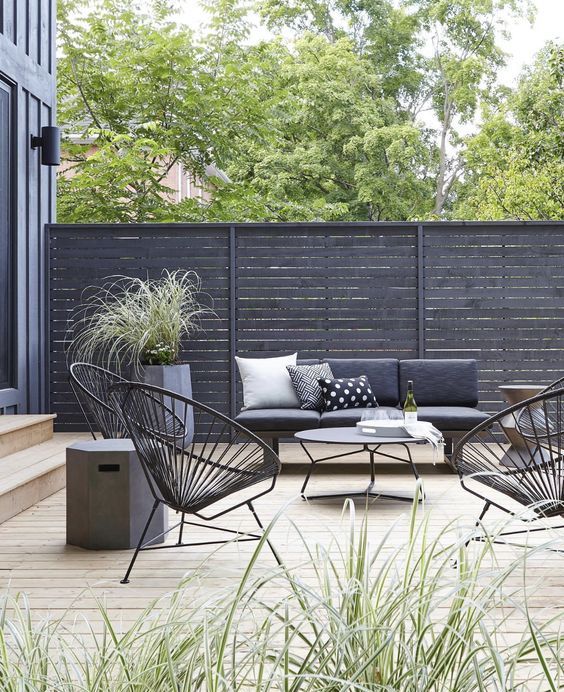 a black fence with a grey sofa and dark chairs, a coffee table, some potted greenery for creating a stylish modern terrace