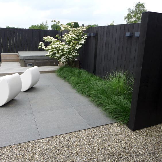 a black fence with grasses and a blooming tree along it are a super stylish combo for a modern or minimalist space