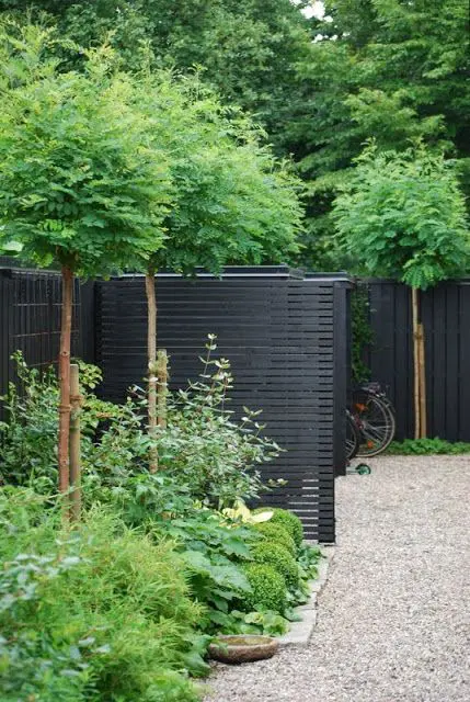 a black fence with greenery and green trees are a fresh and lovely combo that is great for a modern outdoor space