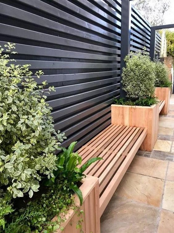 a black wooden fence lined up with a stained bench and planters with greenery are a cool combo for a modern space