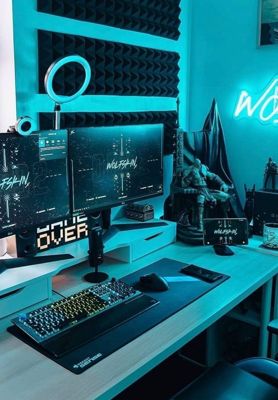 a blue gaming desk setup with sound-proof panels, neon lights, a PC, some bold decor and some more devices is wow