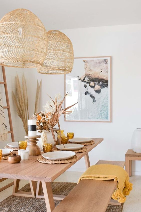 a boho dining room with a stained table and benches, woven pendant lamps, some art, a ladder and a jute rug