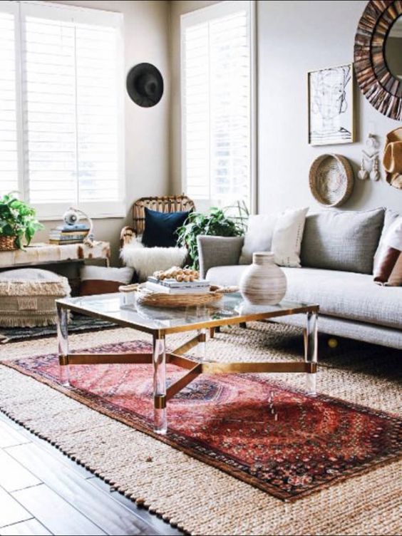 a boho living room with a grey sofa, layered rugs including a jute one, a coffee table, a rattan chair, a bench and some boho poufs