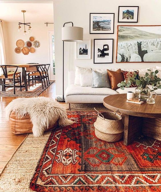 a boho living room with layered rugs including a boho one, a neutral sofa with pillows, a gallery wall, a coffee table with some decor