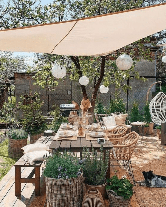 a boho meets farmhouse terrace with a stained table and bench, rattan chairs and a loveseat, potted greenery and plants