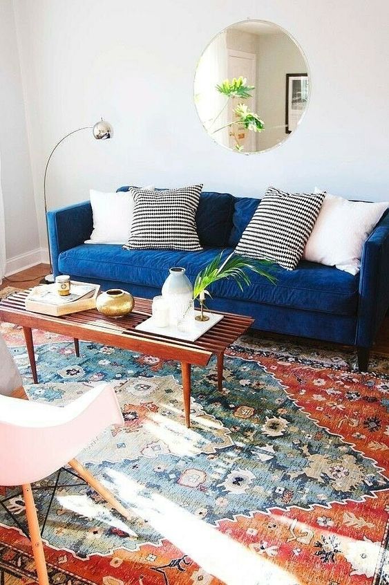 a boho modern living room with a bright printed rug, a navy sofa and pillows, a neutral chairs, a coffee table with some lovely decor