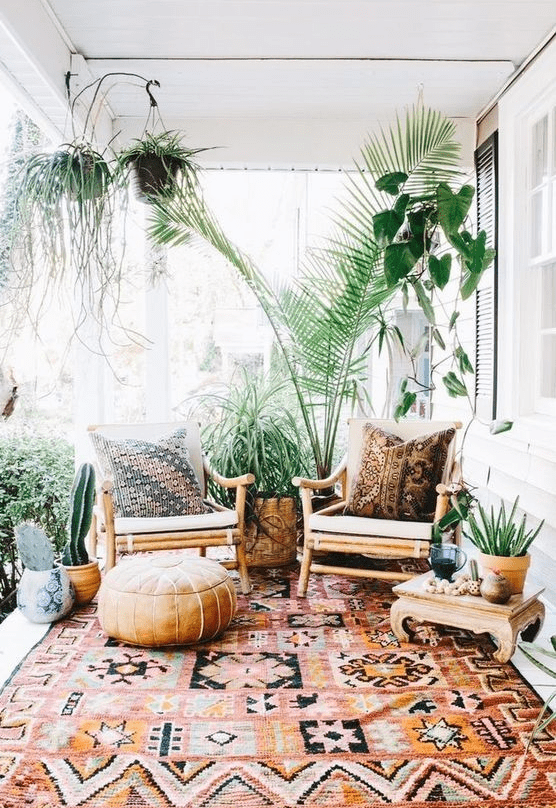 a boho porch with rattan and wooden furniture, printed textiles, potted greenery and cacti is very welcoming