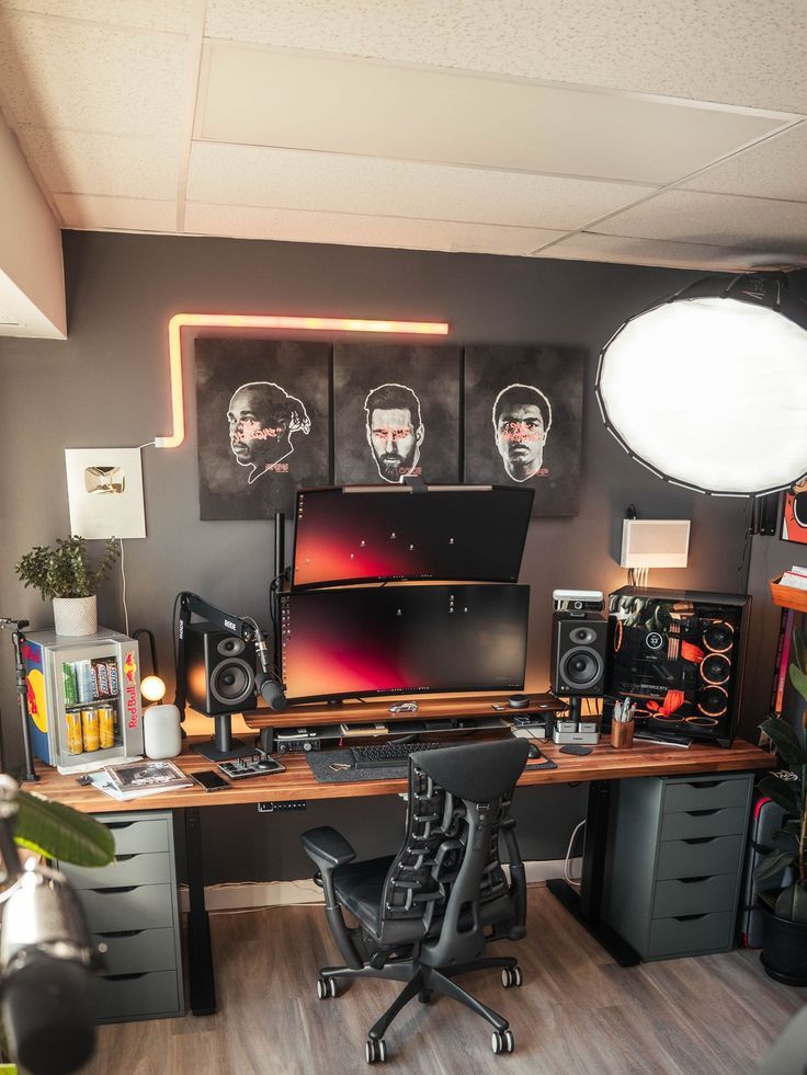 a modern industrial gaming setup with artwork, a desk, some screens and a PC, a black chair, decor and greenery is wow