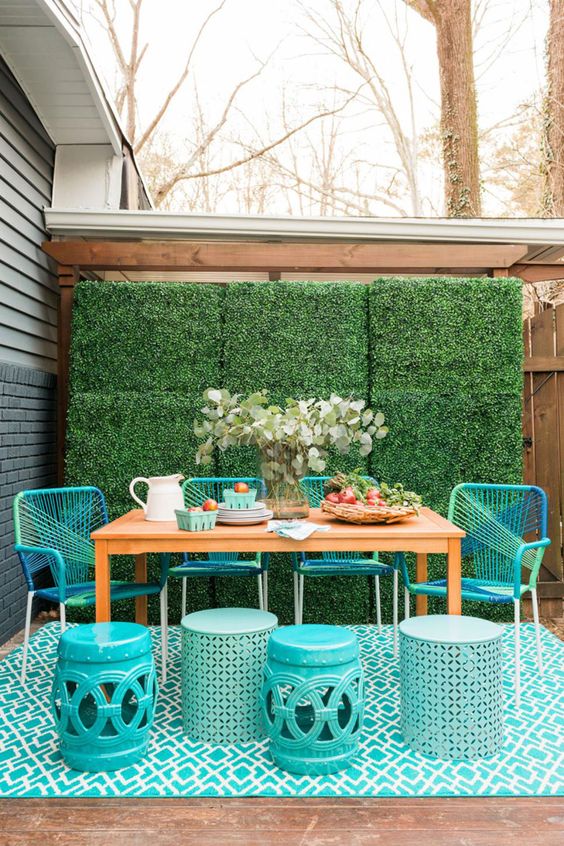 a bold outdoor dining space with a living wall, a stained table, turquoise chairs and side table, a matching rug and some greenery