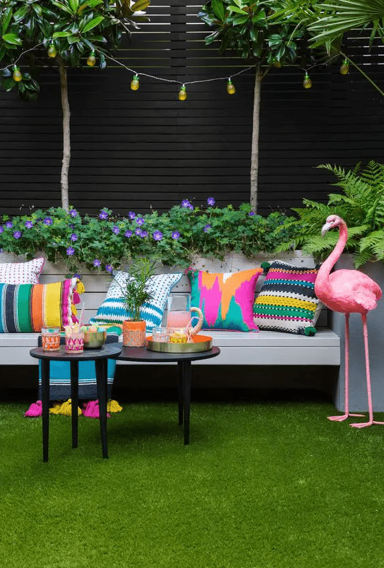 a bold terrace with a green lawn, a sofa with colorful pillows, side tables with bold tableware and a bold pink flamingo