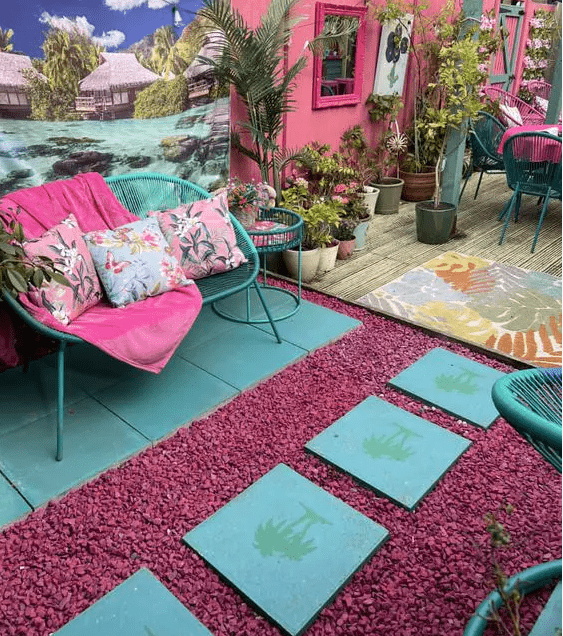 a bold terrace with fuchsia gravel and blue tiles, emerald furniture and colorful printed pillows is wow