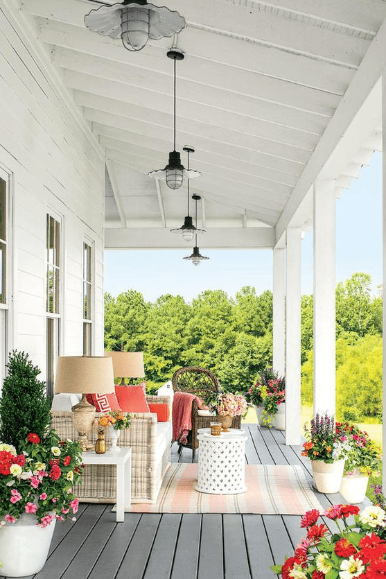 a bright and cool farmhouse porch with a white wicker sofa, potted blooms and plants, side tables and pendant and table lamps