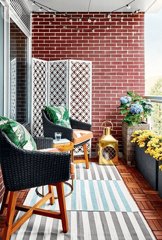 a bright and stylish balcony with layered rugs, wicker chairs and printed pillows, potted blooms and a large candle lantern