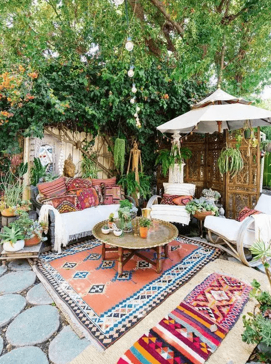 a bright boho summer terrace with a white sofa, printed pillows, rockers, printed rugs, a metal table and potted greenery and plants