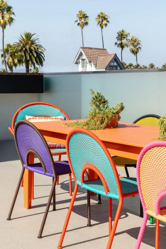 a bright outdoor dining space with an orange table, colorful chairs and some greenery is amazing for a modern terrace