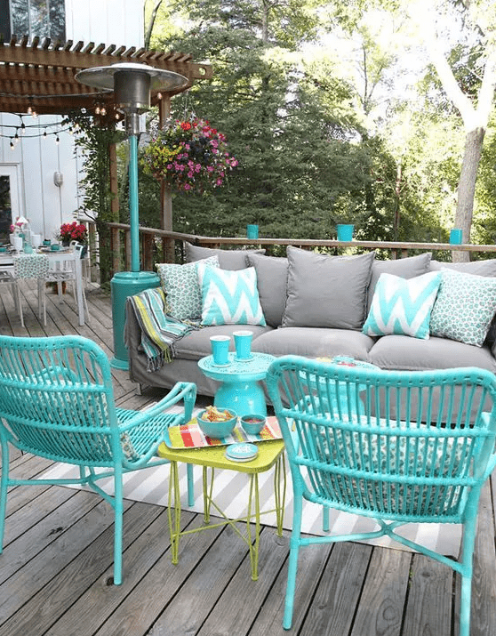 a bright outdoor living room with a grey sofa, turquoise rattan chairs, a green side table and some colorful cushions and pillows