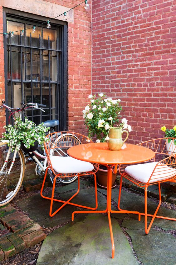 a bright outdoor space with an orange table and chairs, some blooms is a lovely nook to have a coffee in
