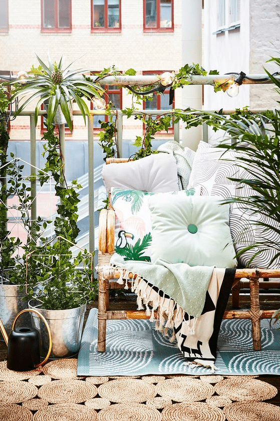 A bright summer balcony with a rattan sofa, printed textiles, potted greenery and layered rugs feels very tropical like