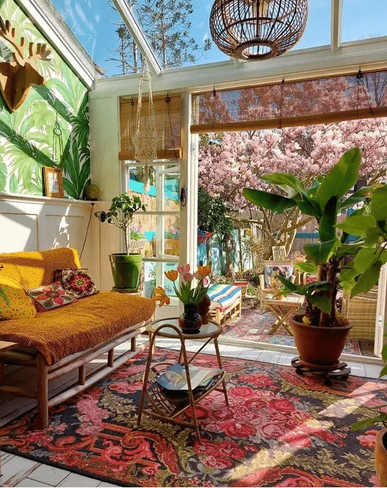a bright terrace with a colorful printed rug, a marigold loveseat, bold pillows, potted plants and blooms