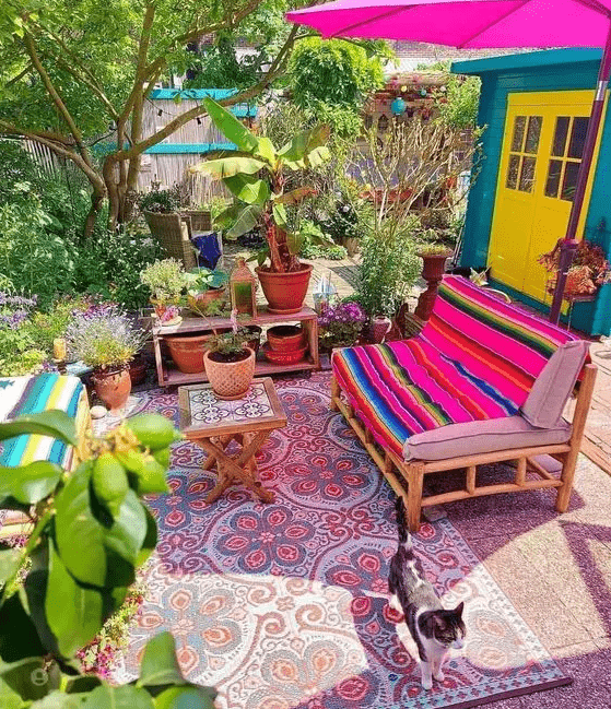 a bright terrace with a hot pink umbrella, a bold loveseat, printed rugs, potted greenery and blooms