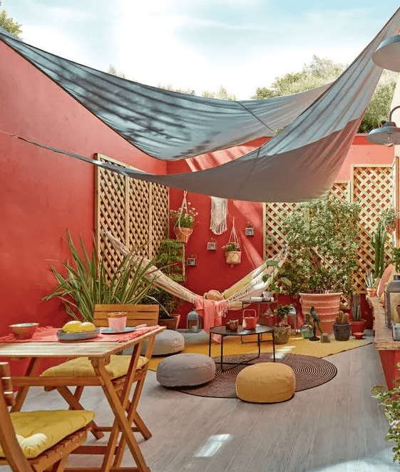 a bright terrace with red walls, folding furniture, poufs, potted greenery and plants is a chic space