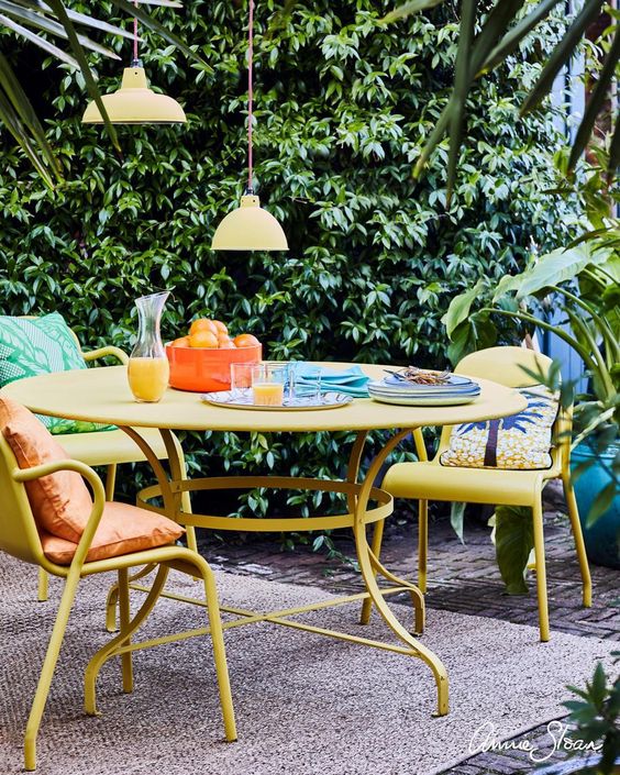 a bright tropical terrace with a yellow table and chairs, yellow pendant lamps and some bold pillows and a lilac rug