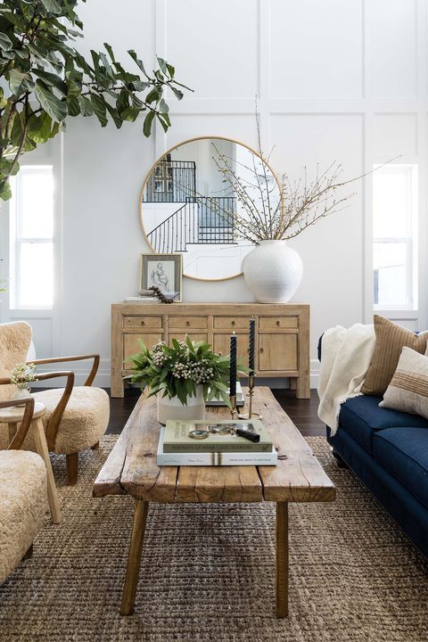 a chic coastal living room with a jute rug, boucle chairs, a navy sofa with pillows, a reclaimed table with decor and a credenza with chic decor