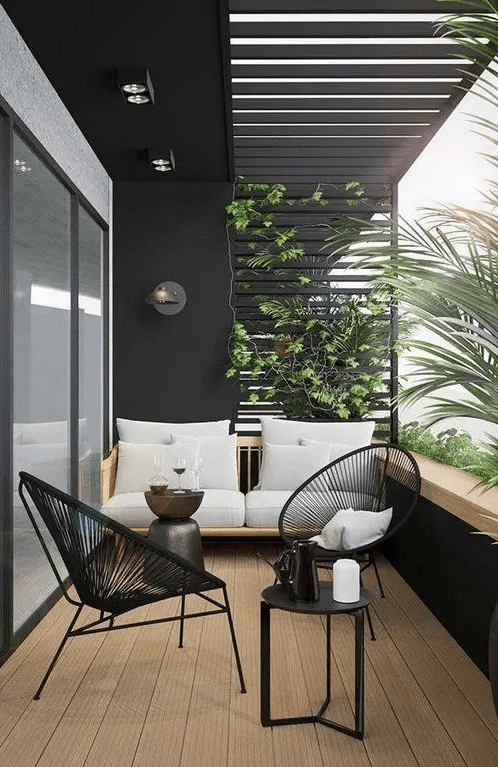 a chic modern balcony done in black and white, with a neutral stained sofa, black chairs, a black round table and lots of greneery