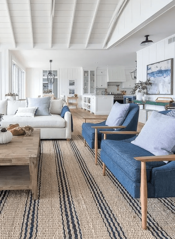 a coastal living room with a neutral sofa and blue chairs, a stained coffee table, neutral pillows and a striped jute rug