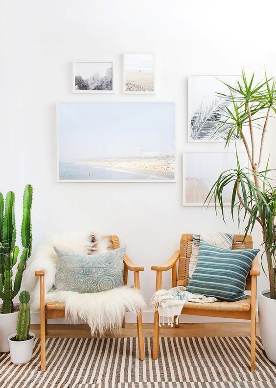 a coastal space with a striped rug, woven chairs and pillows, a gallery wall and potted plants is cozy and cool