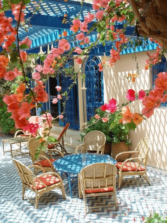 a colorful Mediterranean terrace with blue tiles, wicker chairs, a blue table and bright blooms all around