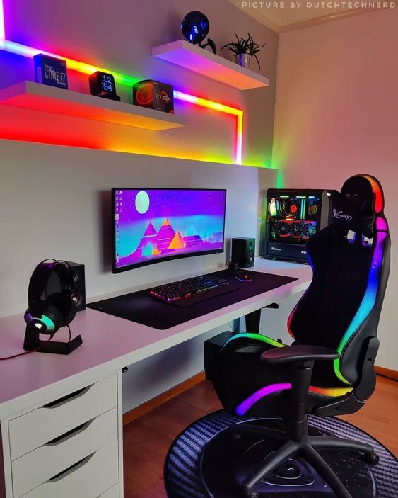 a colorful gaming setup with a deks, a black chair, colorful neon lights, shelves with decor and some devices