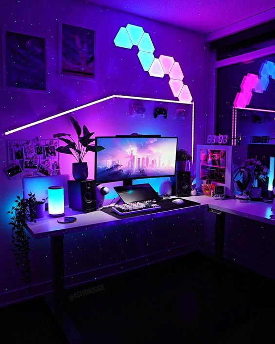 a colorful gaming setup with bold lights on the wall and desk, a PC and some more devices, potted plants and artwork on the wall