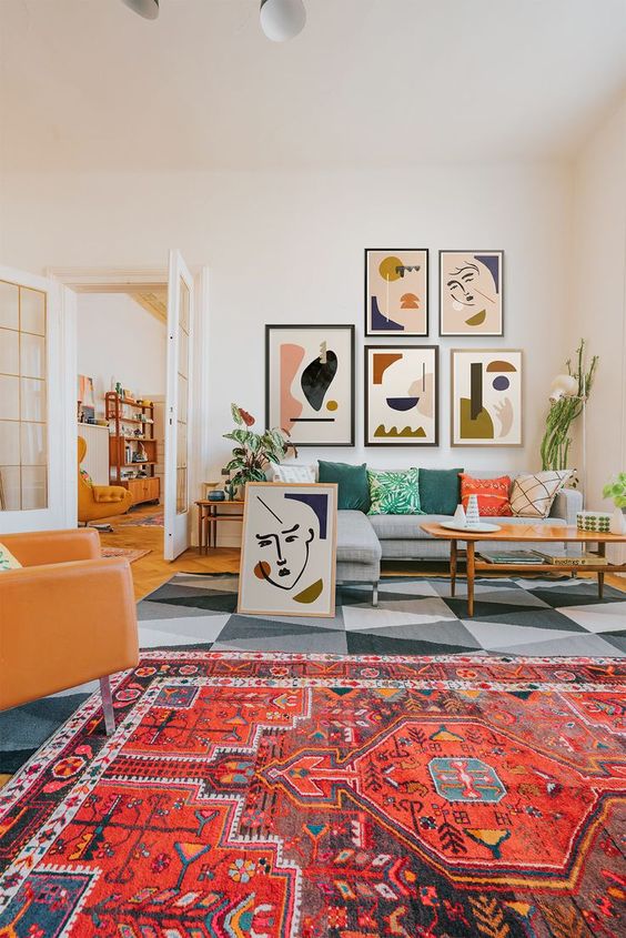 a colorful modern living room with a bold boho and geometric rug, a grey sofa with pillows, a modern gallery wall and an amber leather chair