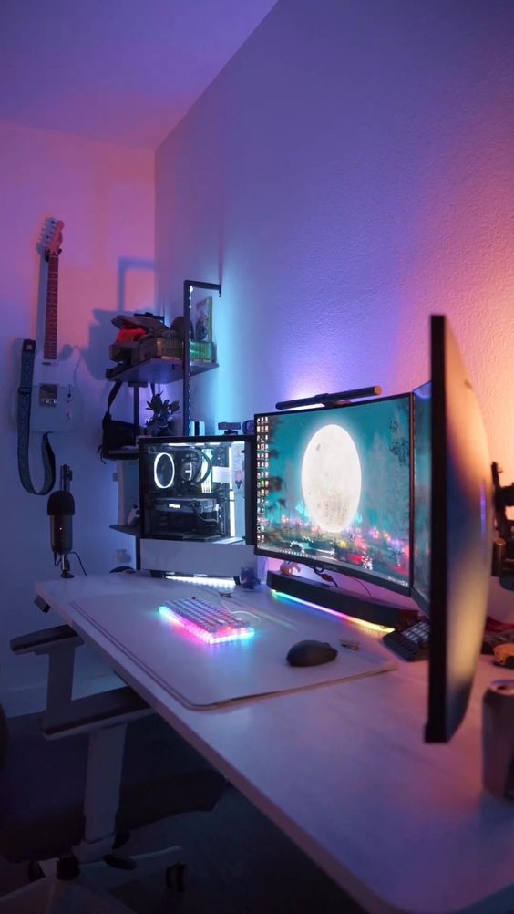 a colorful neon gaming corner with screens and a PC, a lit up keyboard, a desk and a chair, a shelving unit and a guitar on the wall