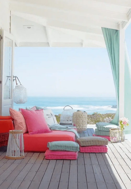 a colorful summer seaside terrace with a bright daybed, colorful pillows and cushions and candle lanterns