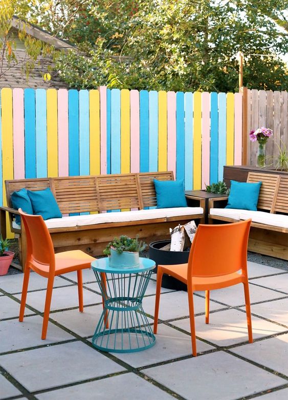 a colorful terrace with a bright fence, stained sofas with blue pillows, orange chairs, a side table in blue and a fire pit