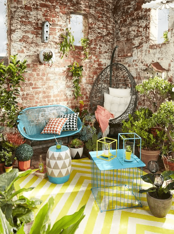 a colorful terrace with bold blue furniture, a printed yellow rug and a matching chevron side table, potted greenery and candle lanterns is fun