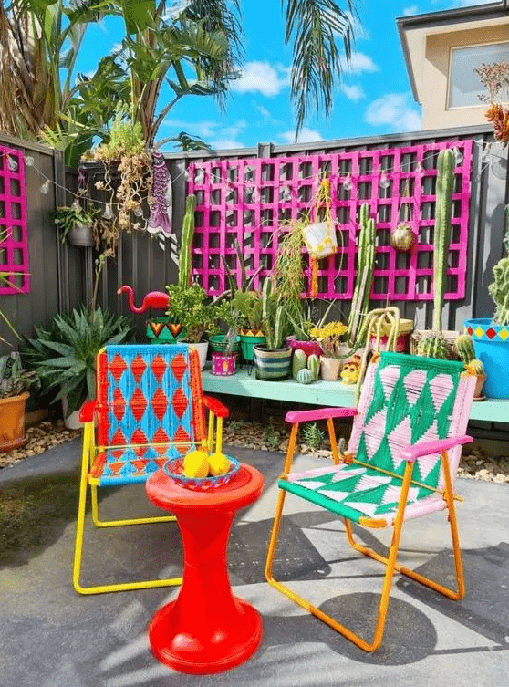 a colorful terrace with hot pink frames, an aqua bench with lots of plants, colorful chairs, a red side table and bright decor
