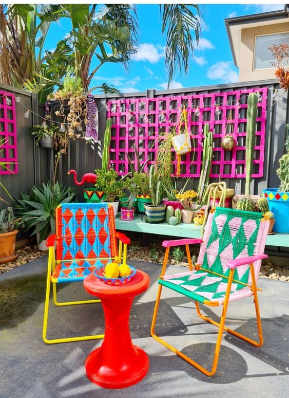 a colorful terrace with hot pink frames, an aqua bench with potted cacti, super colorful chairs and a red side table